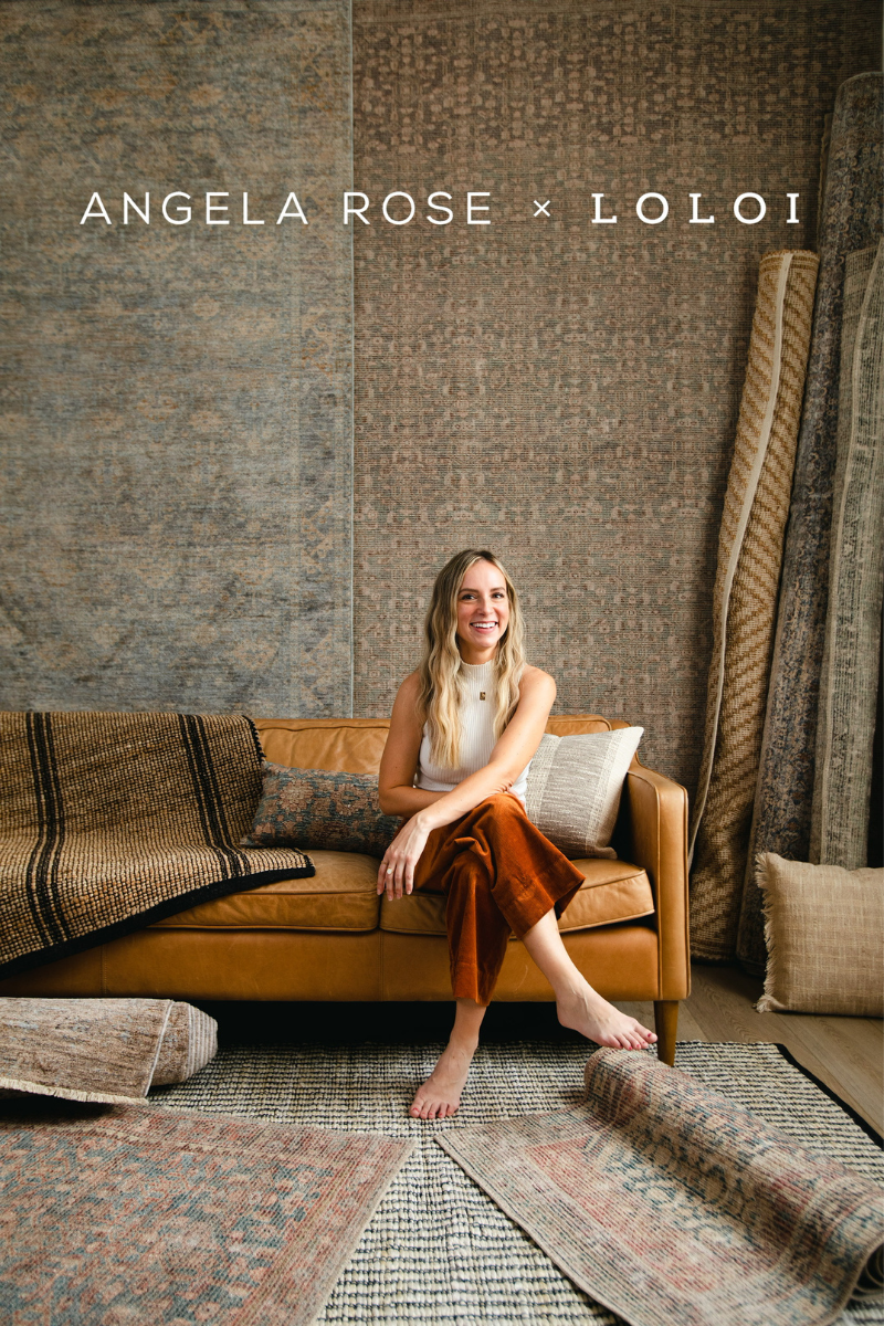 Angela Rose x Loloi area rug collection displayed in a showroom with Angela Rose on a leather sofa surrounded by traditional patterned Area Rugs.