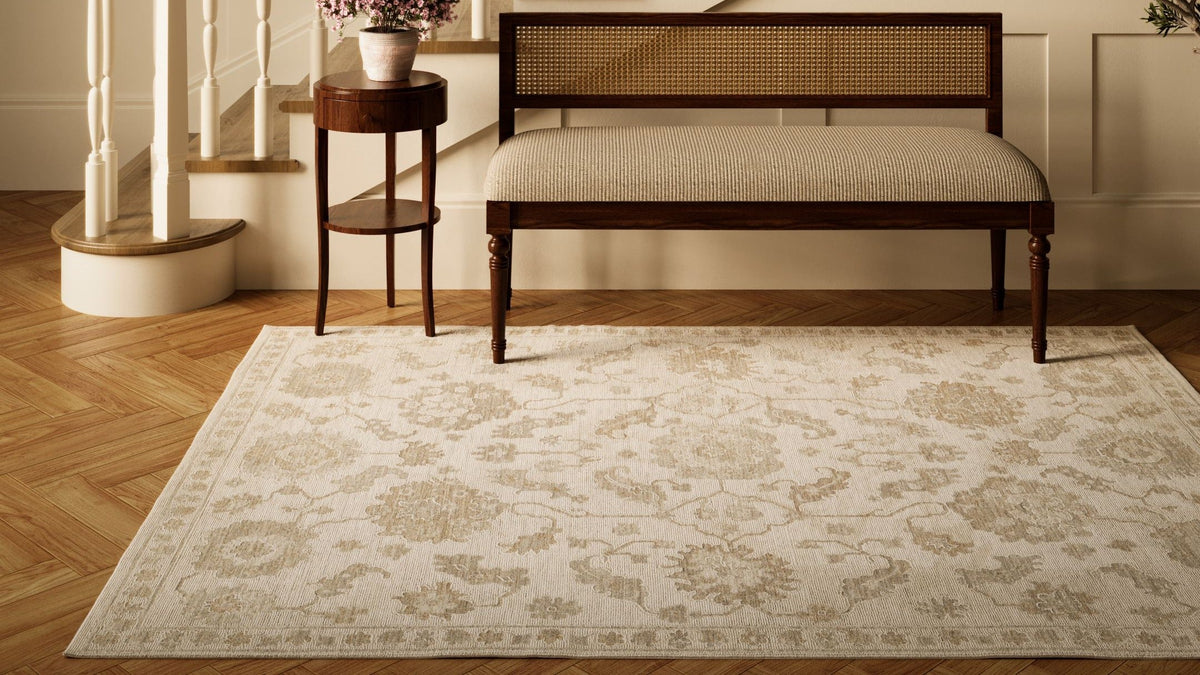 Cream and beige Momeni Ansel rug with classic pattern under a wooden bench on herringbone hardwood floor.