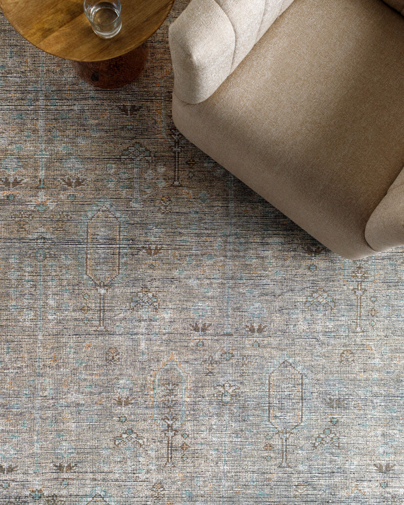 Distressed vintage-style Darling rug in neutral tones with subtle blue accents, styled under a beige sofa and wooden side table.