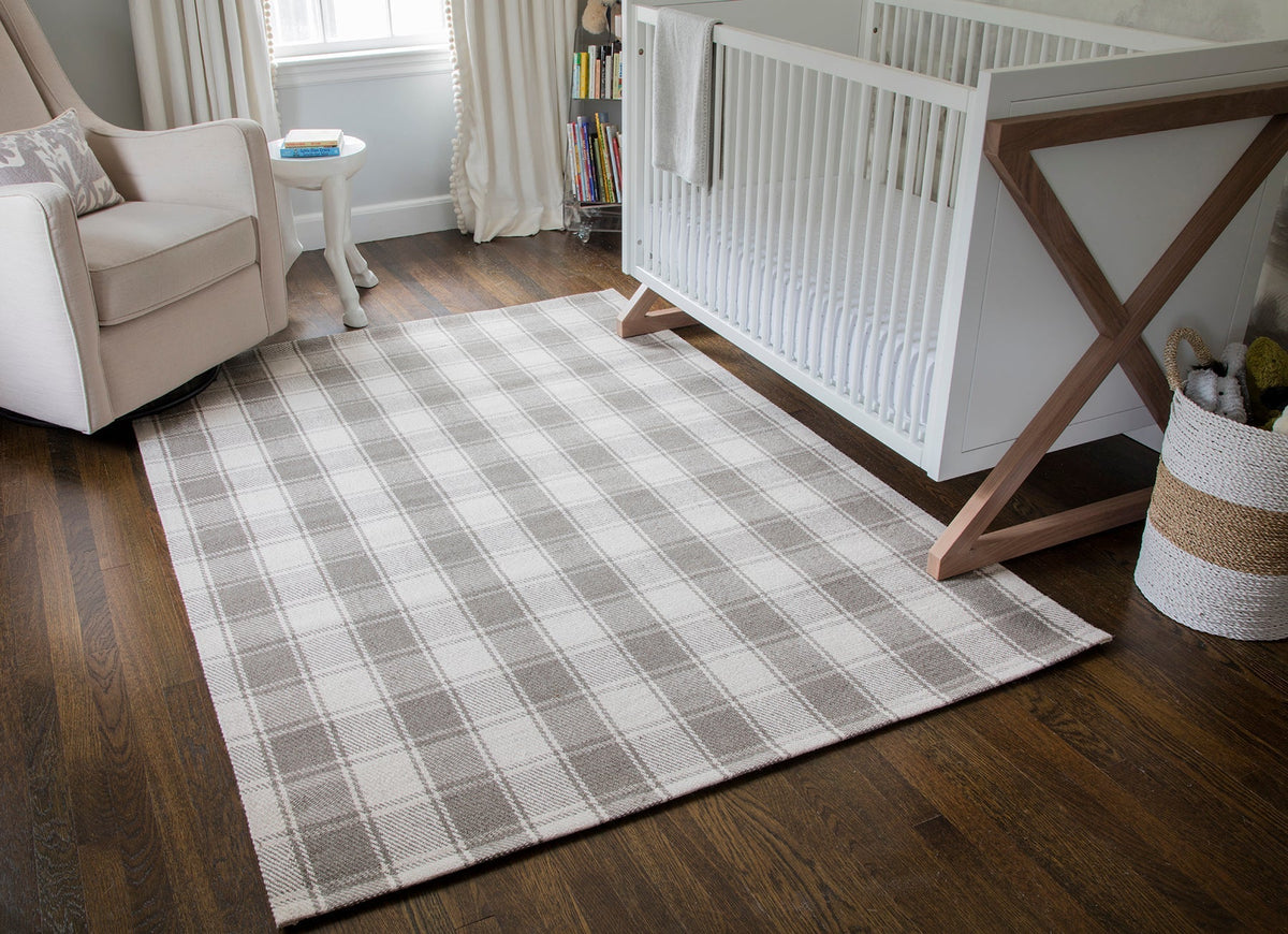 Erin Gates by Momeni Marlborough grey and white tartan plaid rug on dark wood floor beside a white crib and beige rocking chair in a nursery.