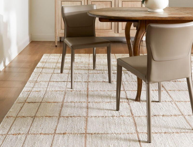 Becki Owens x Livabliss Kamey handmade rug with beige grid pattern in a farmhouse dining room featuring leather chairs and light wood sideboard.