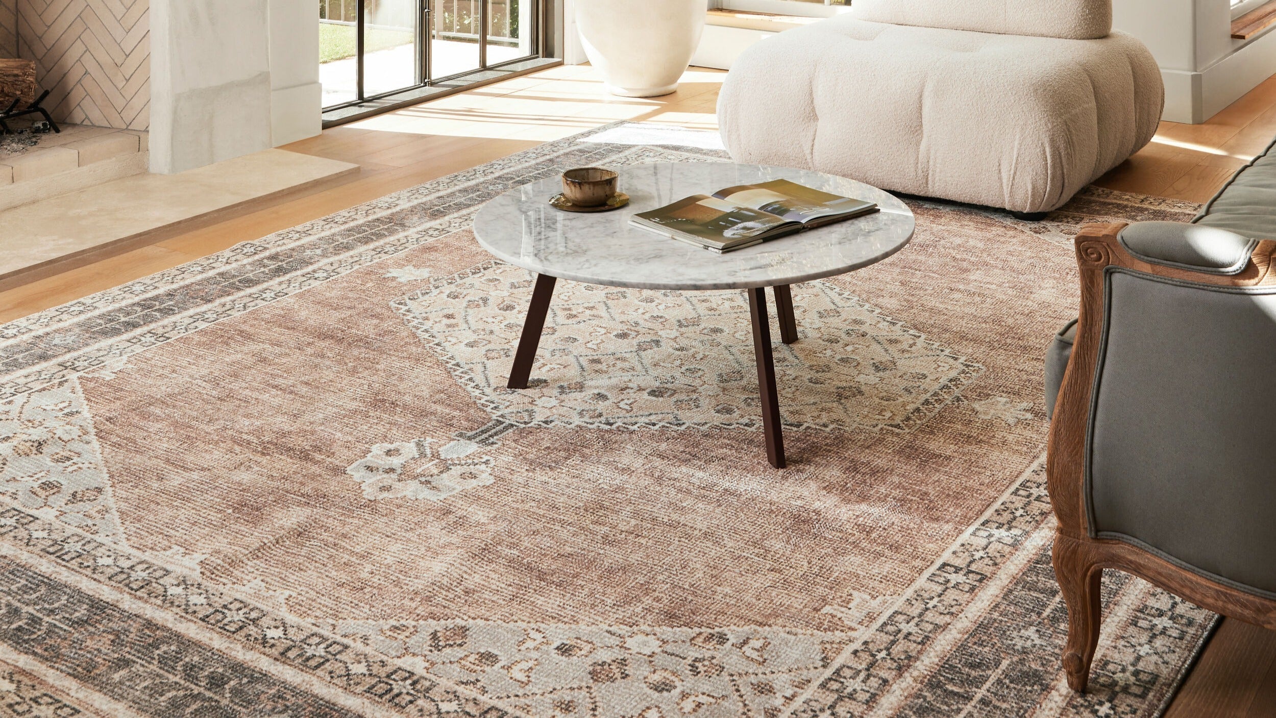 Becki Owens x Livabliss Lila Rug in warm tones featuring a traditional pattern beneath a round marble coffee table in a sunlit living room.
