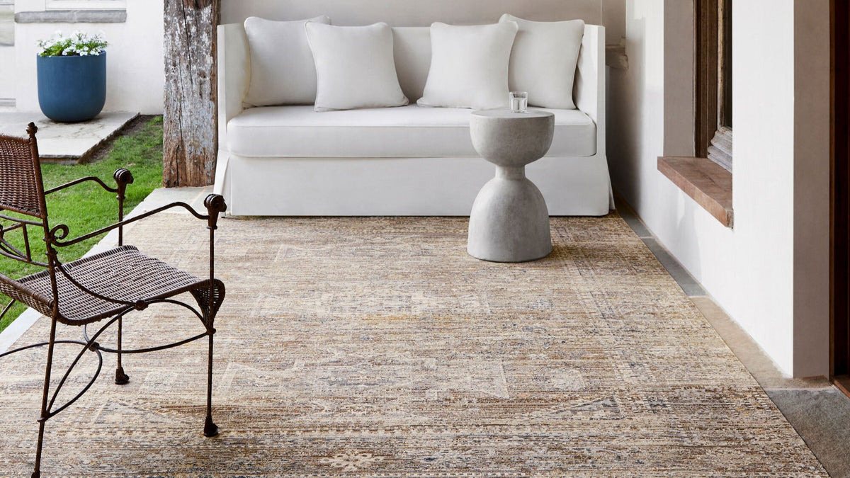 Becki Owens Margaret rug in neutral tones laid on a patio with a white sofa, concrete side table, and wrought iron chair.