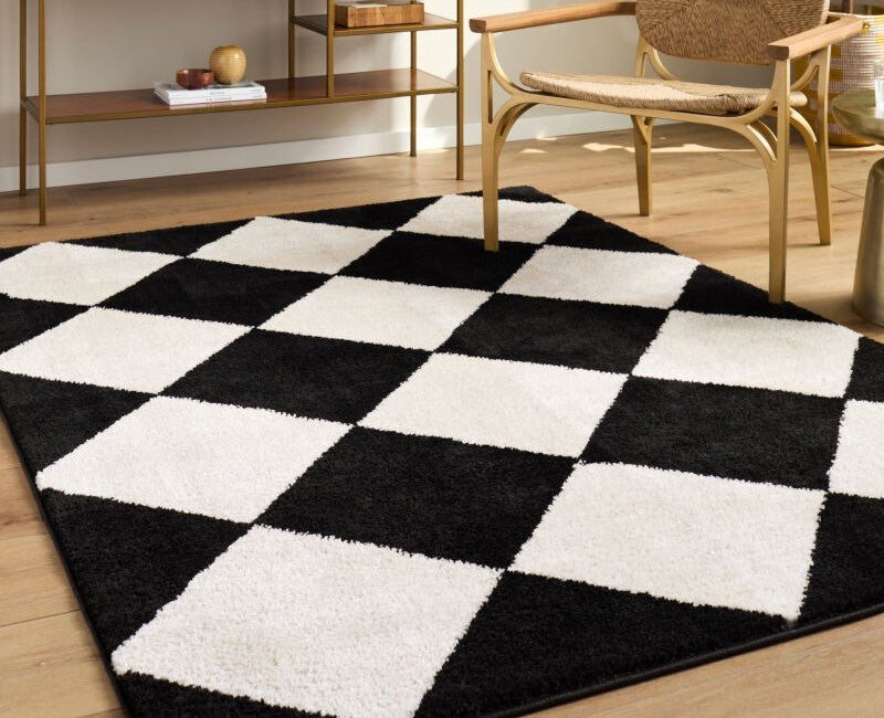 Elle Decor X Livabliss Black and white diamond patterned Rivoli rug on hardwood floor beside mid-century chair and gold shelving unit.