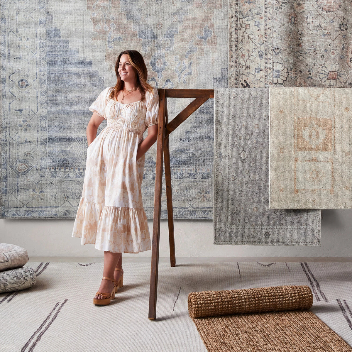 Becki Owens x LIVABLISS area rug collection featuring designer Becki Owens, surrounded by vintage-inspired rugs in soft ivory, gray, beige, and blush tones. Discover elegant floral patterns, subtle geometric designs, and natural textures that bring timeless style and understated sophistication to any room at Rug-Resources.com.