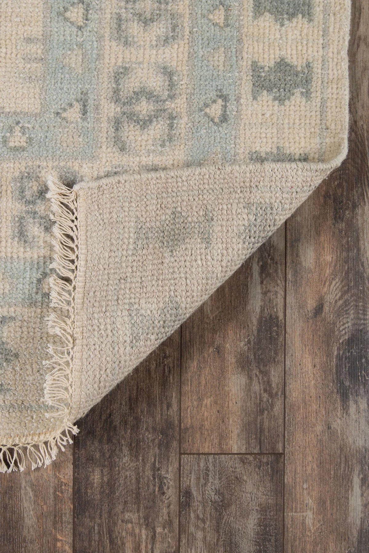Erin Gates x Momeni Concord CRD-2 Sudbury ivory area rug corner folded to reveal textured wool backing, geometric pattern, and fringe on dark wood flooring.