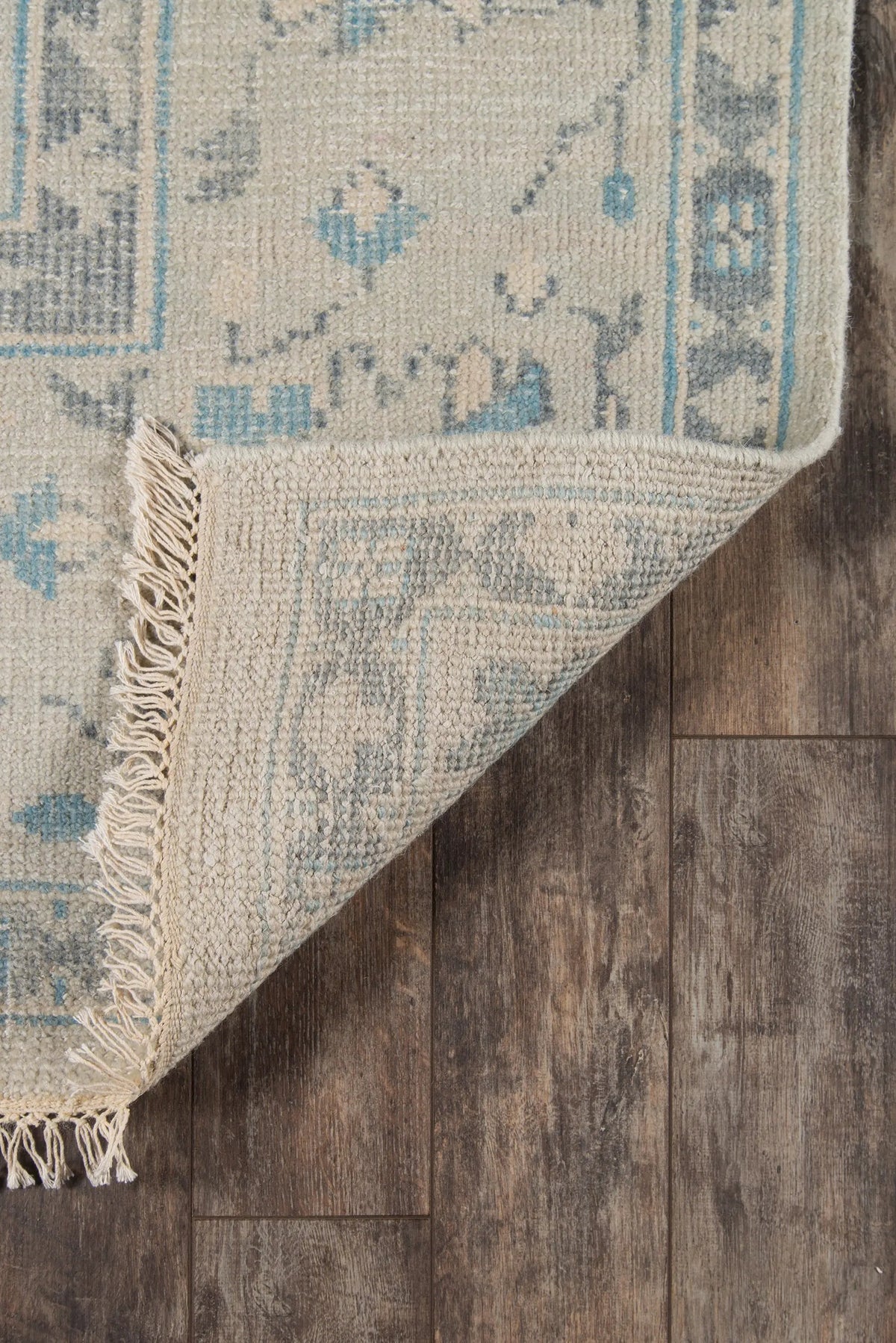 Erin Gates by Momeni Concord CRD-3 (Lowell) Ivory Area Rug corner lifted on wood floor, revealing textured weave, blue traditional patterns, and fringed edge.