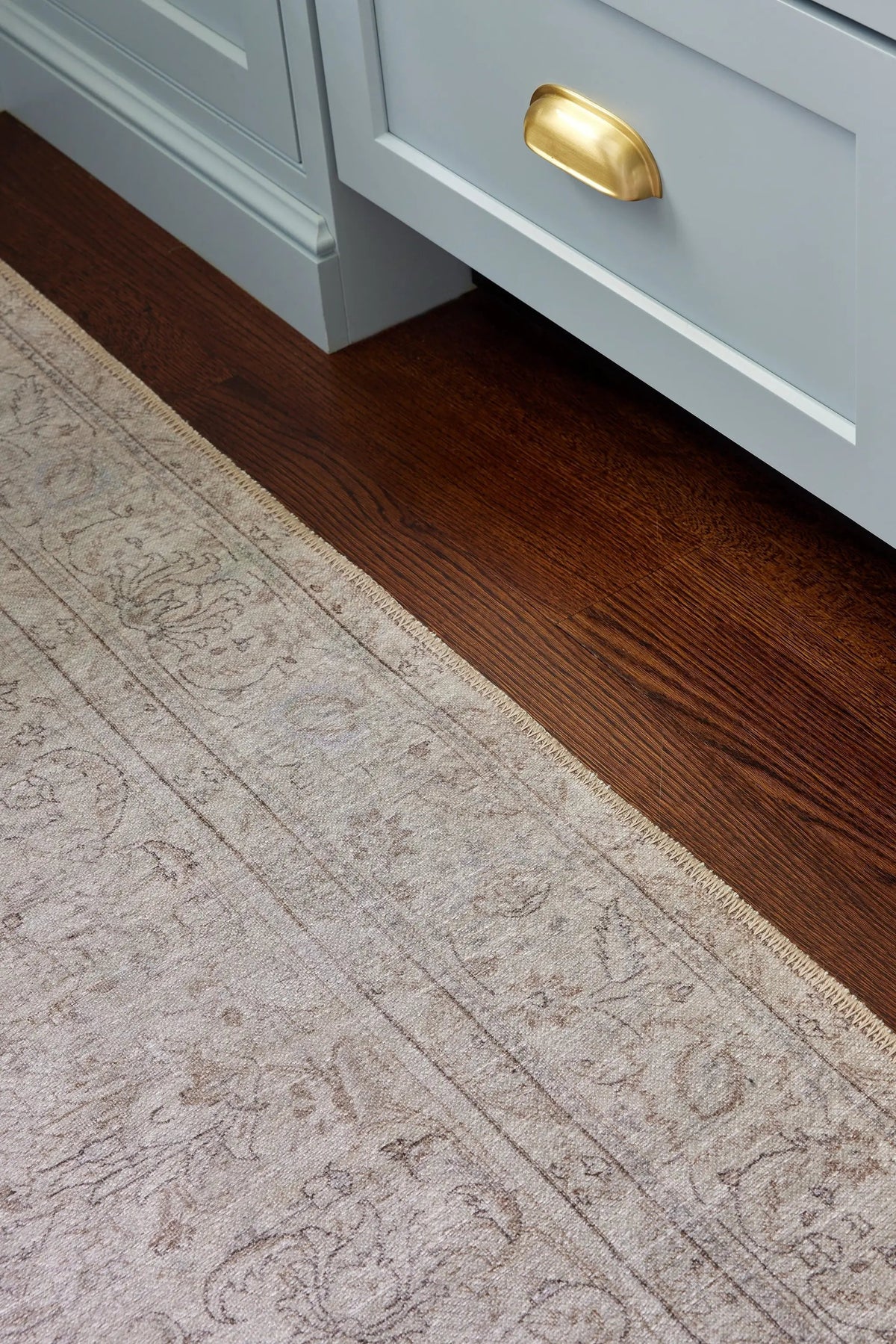 Erin Gates by Momeni Dorset DOR-4 gray area rug with vintage pattern and fringed edge placed on dark hardwood flooring near cabinetry.