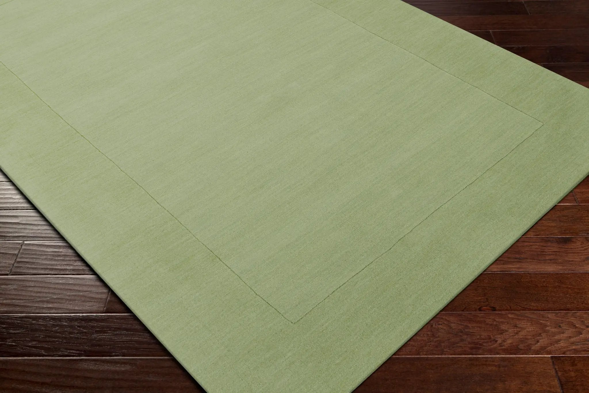 Livabliss Mystique M-310 medium green hand-loomed wool area rug with a refined high-low pile texture and border detail on dark wood flooring.