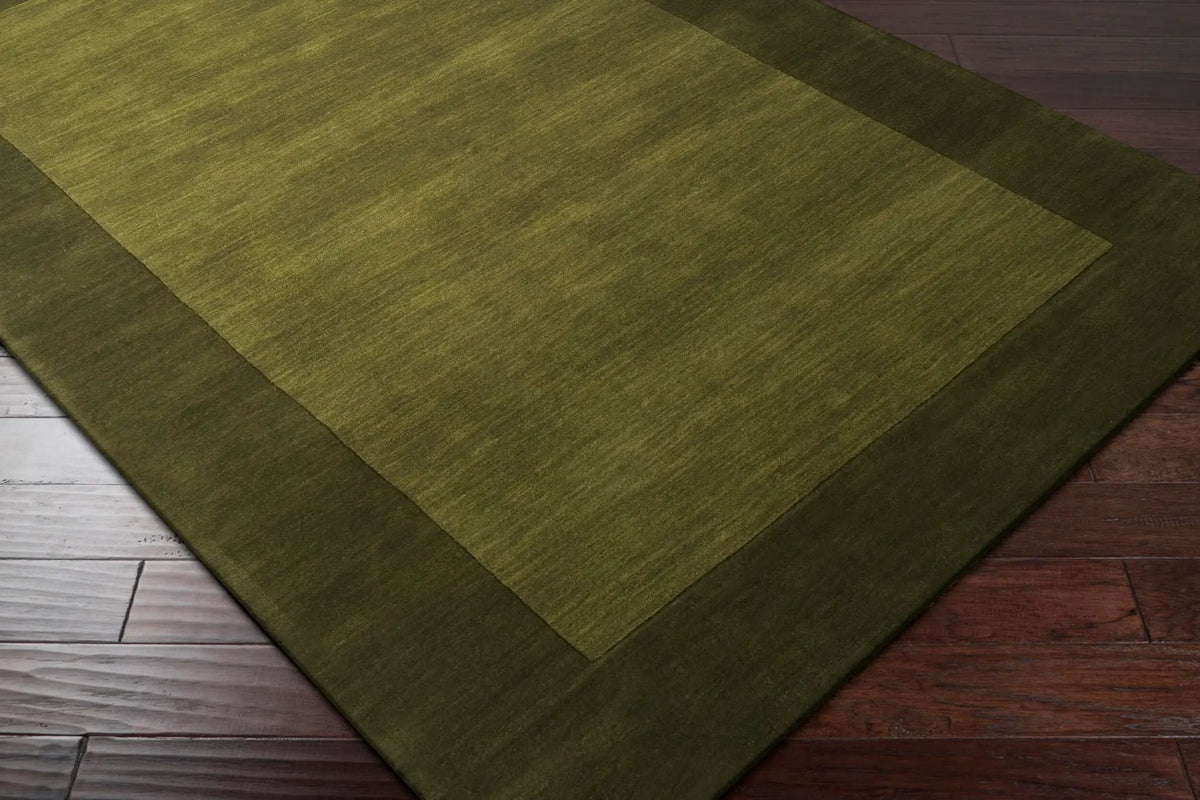 Livabliss Mystique M-315 Olive area rug featuring a two-tone design with a lighter center and darker border, showcasing a textured wool pile on hardwood flooring.