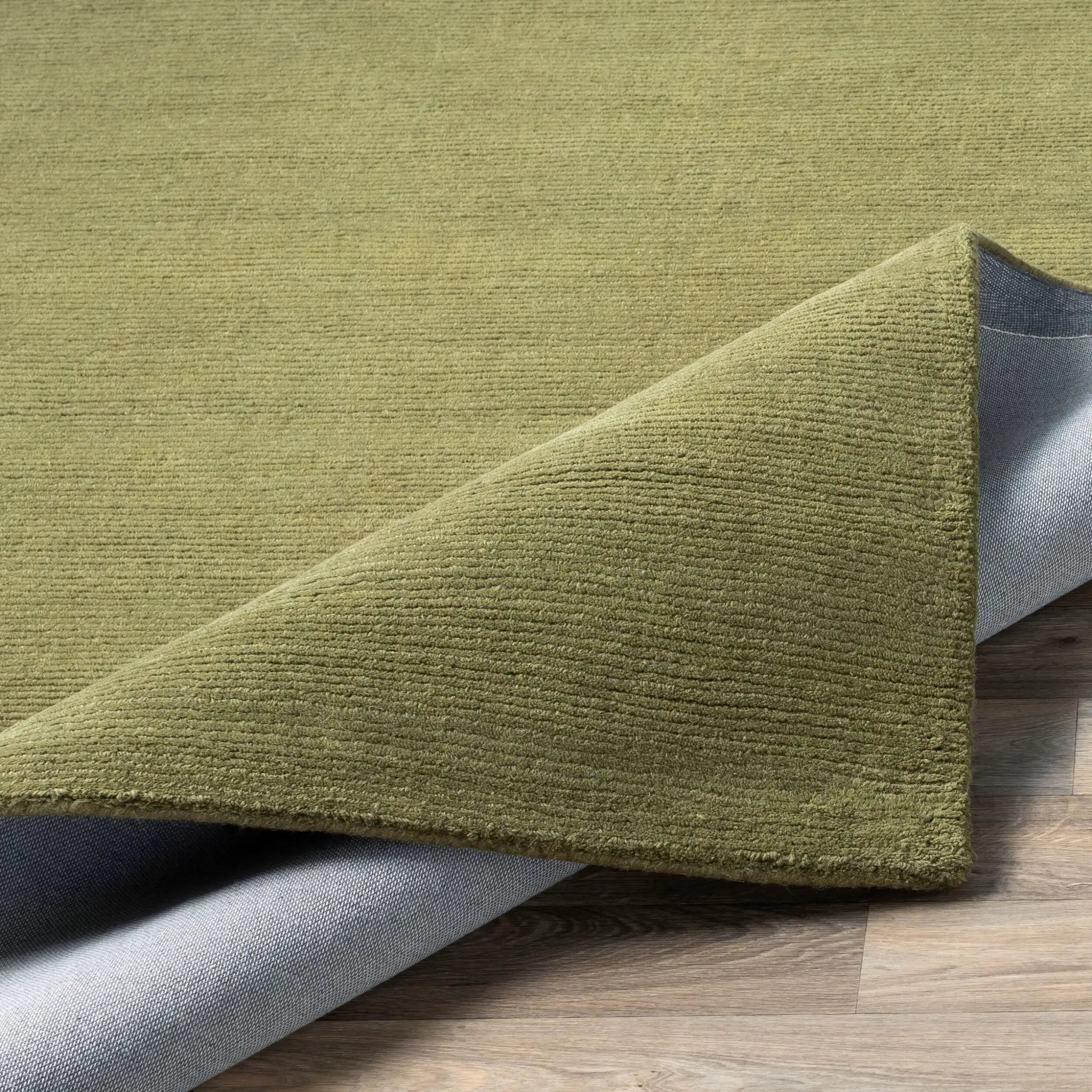 Livabliss Mystique M-329 Sage green wool area rug with sculpted high-low wave texture and a grey backing, corner folded on a wood floor.