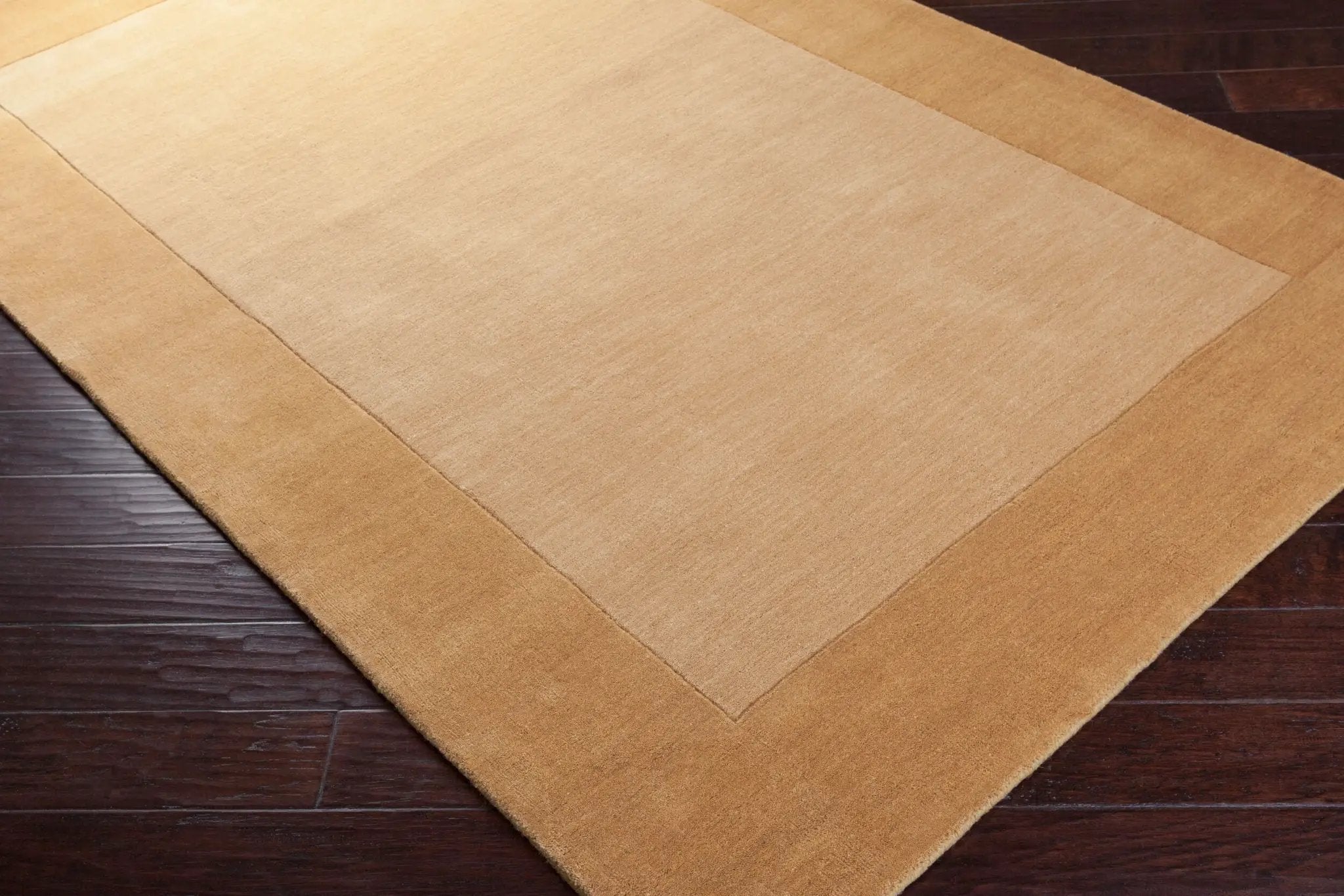 Textured Camel color Livabliss Mystique M-345 area rug with a darker border on dark wood flooring, featuring traditional hand-loomed comfort for modern interiors.