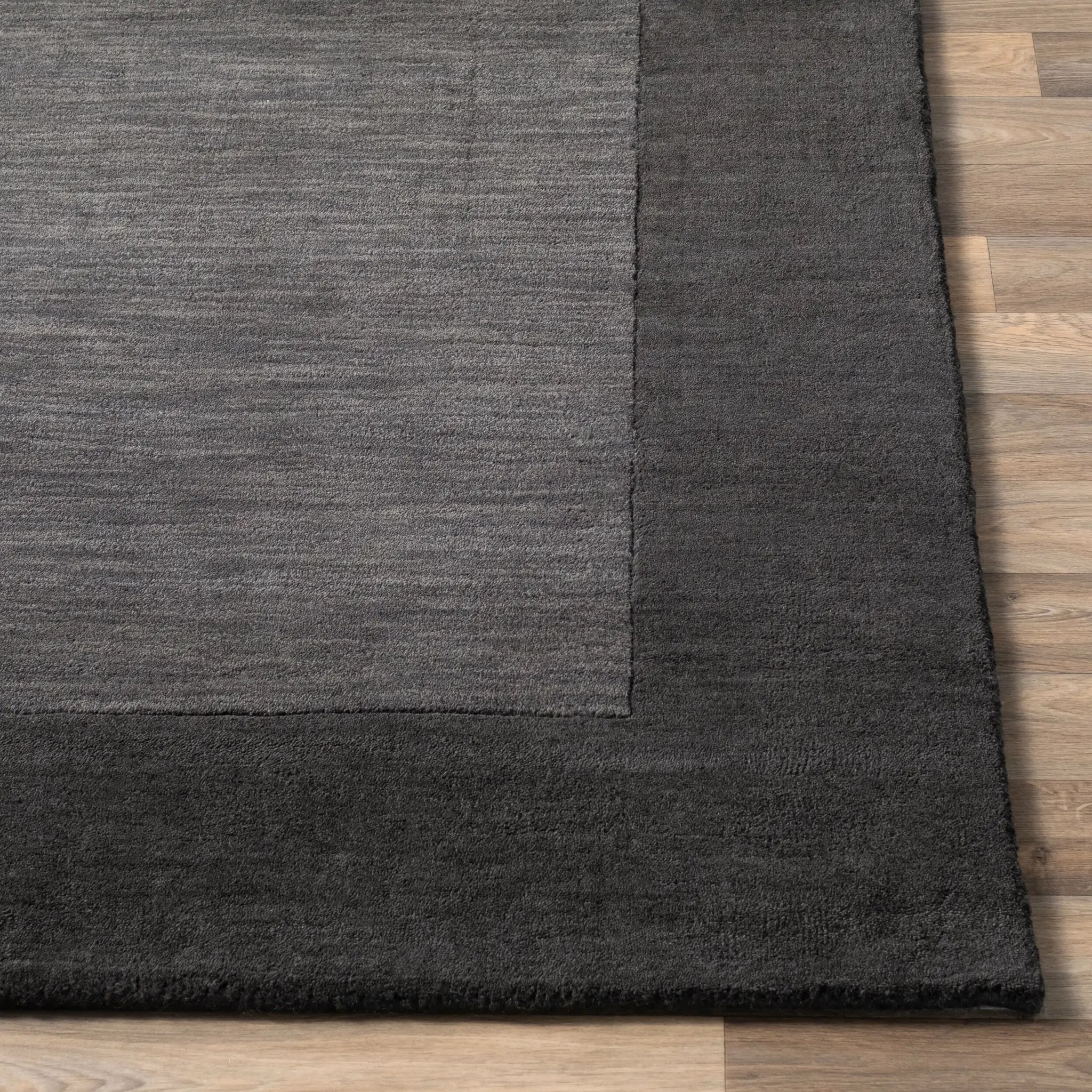Livabliss Mystique M-347 Charcoal area rug with textured center and solid border on wood floor. Durable neutral design for modern living spaces and bedrooms.