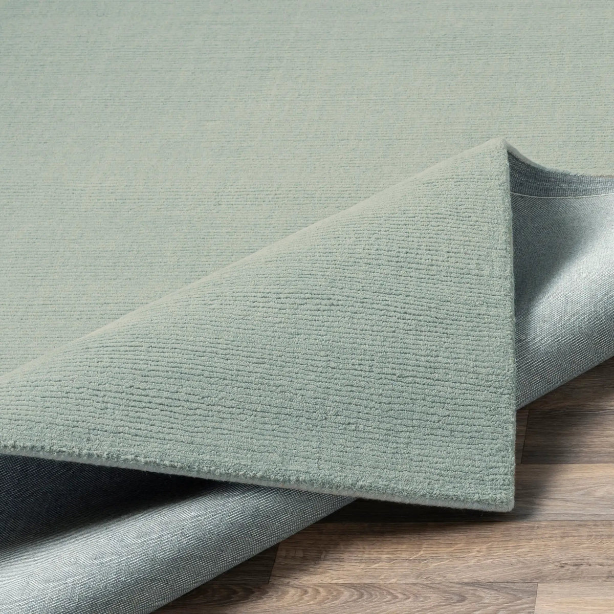 Livabliss Mystique M-5328 dusty sage area rug with textured high-low pile and durable backing, folded corner on wood flooring.