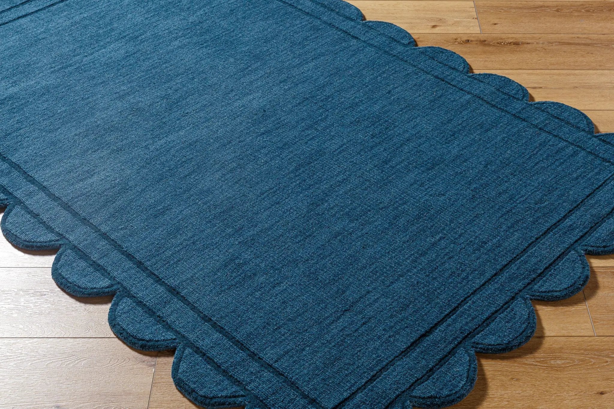 Livabliss Mystique M-5493 Indigo hand loomed wool area rug with scalloped edges and textured weave resting on light hardwood flooring.