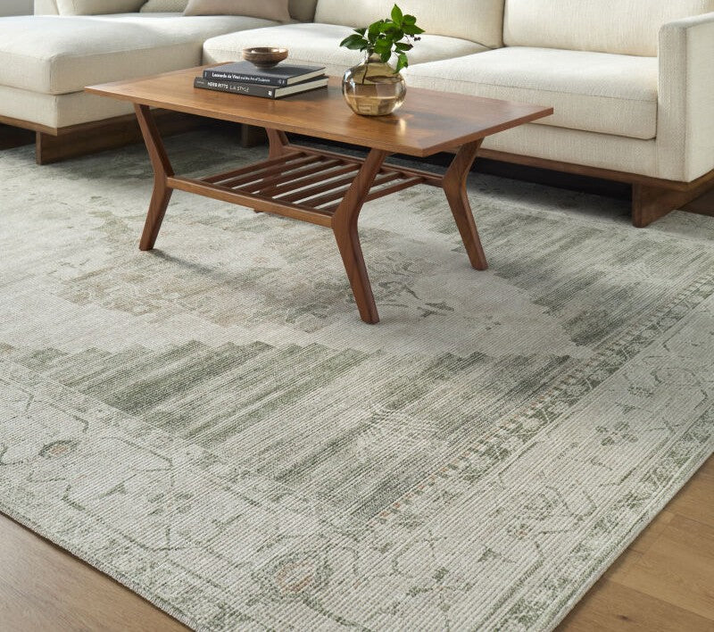 Becki Owen Luca Collection area rug in soft green and beige with a contemporary distressed pattern under a wooden coffee table.