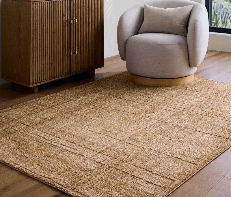 Elle Decor x Livabliss Tan Alma rug with abstract cream lines on hardwood floor, styled under a grey swivel chair and wooden cabinet.