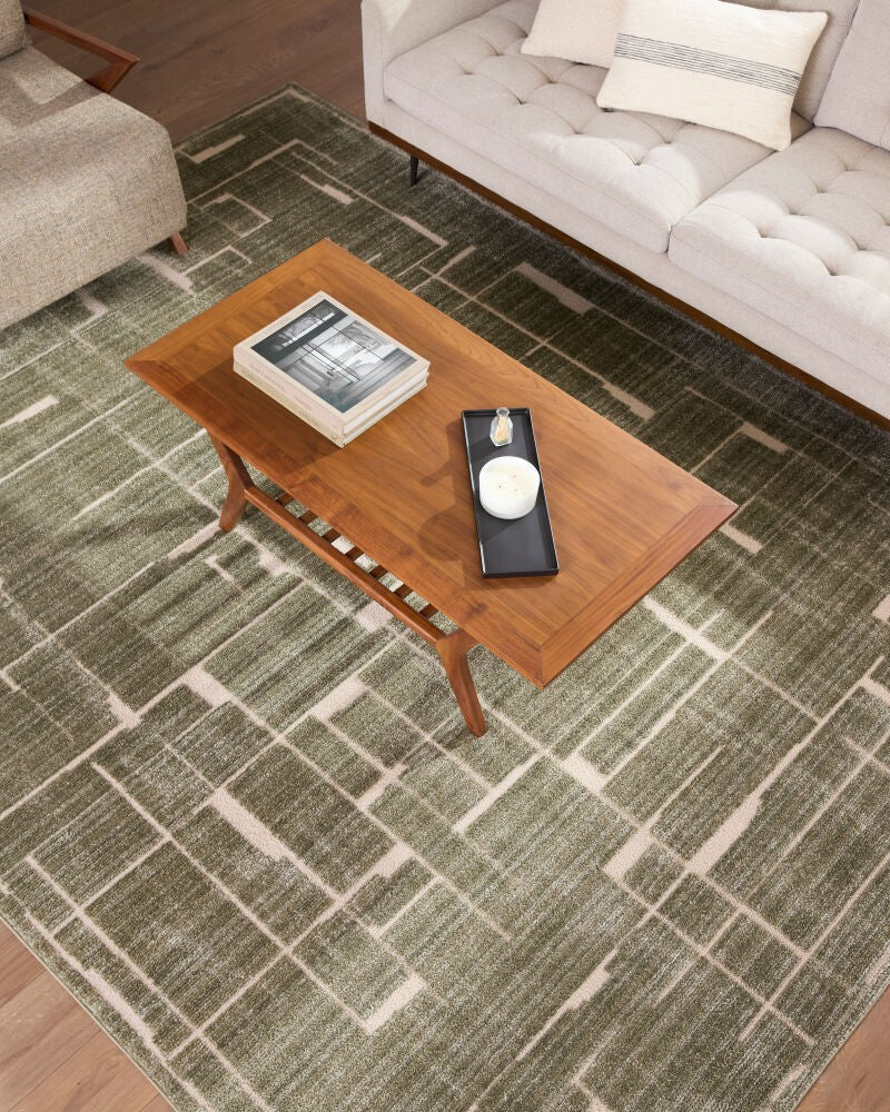 Elle Decor x Livabliss rug collection—featuring a green geometric area rug with neutral tones in a living room. Modern, durable, stain-resistant machine-woven polyester rug styled with a wooden coffee table.