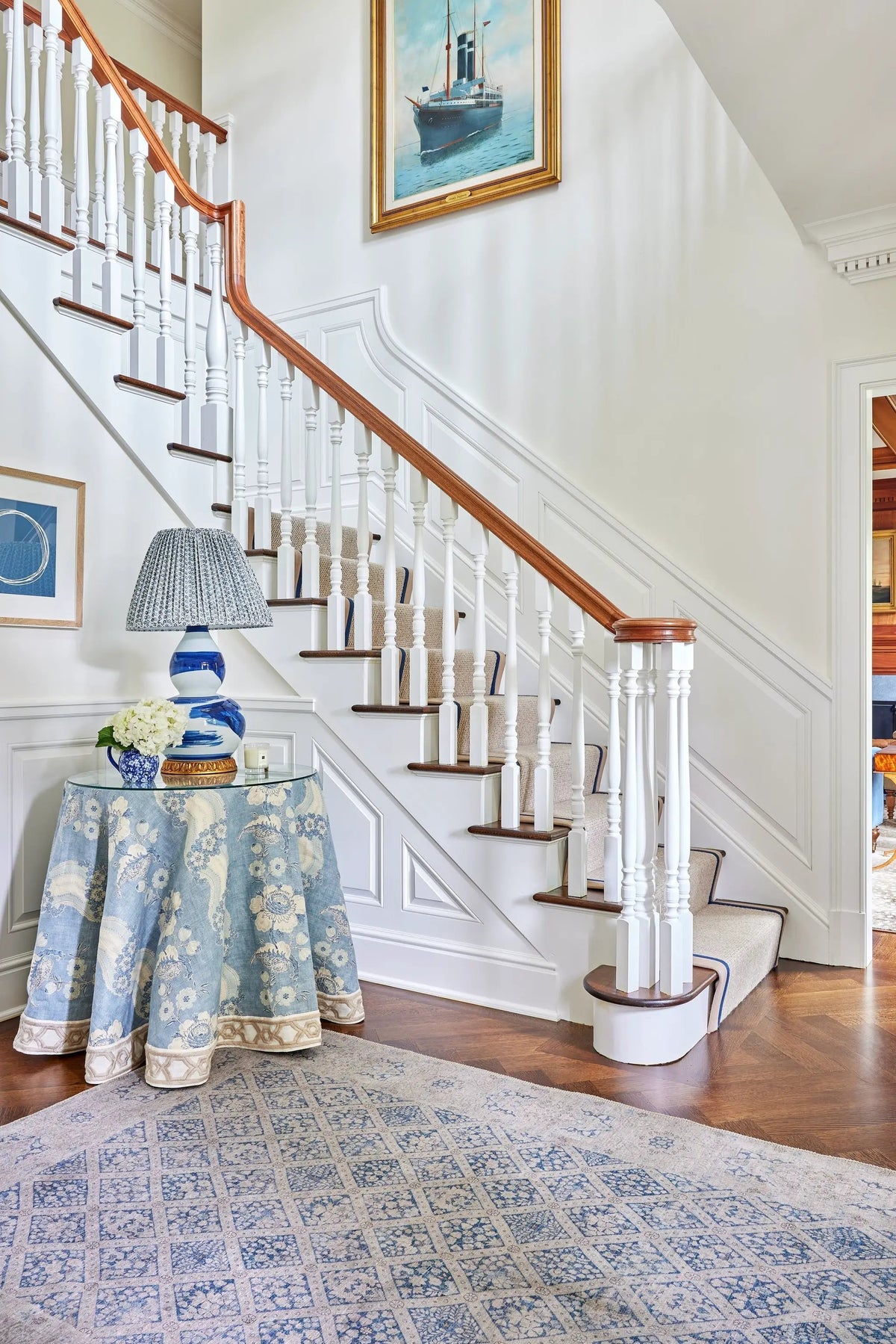 Erin Gates by Momeni Dorset DOR-3 blue geometric patterned area rug in a bright entryway featuring white stairs, wood railing, and a floral tablecloth.