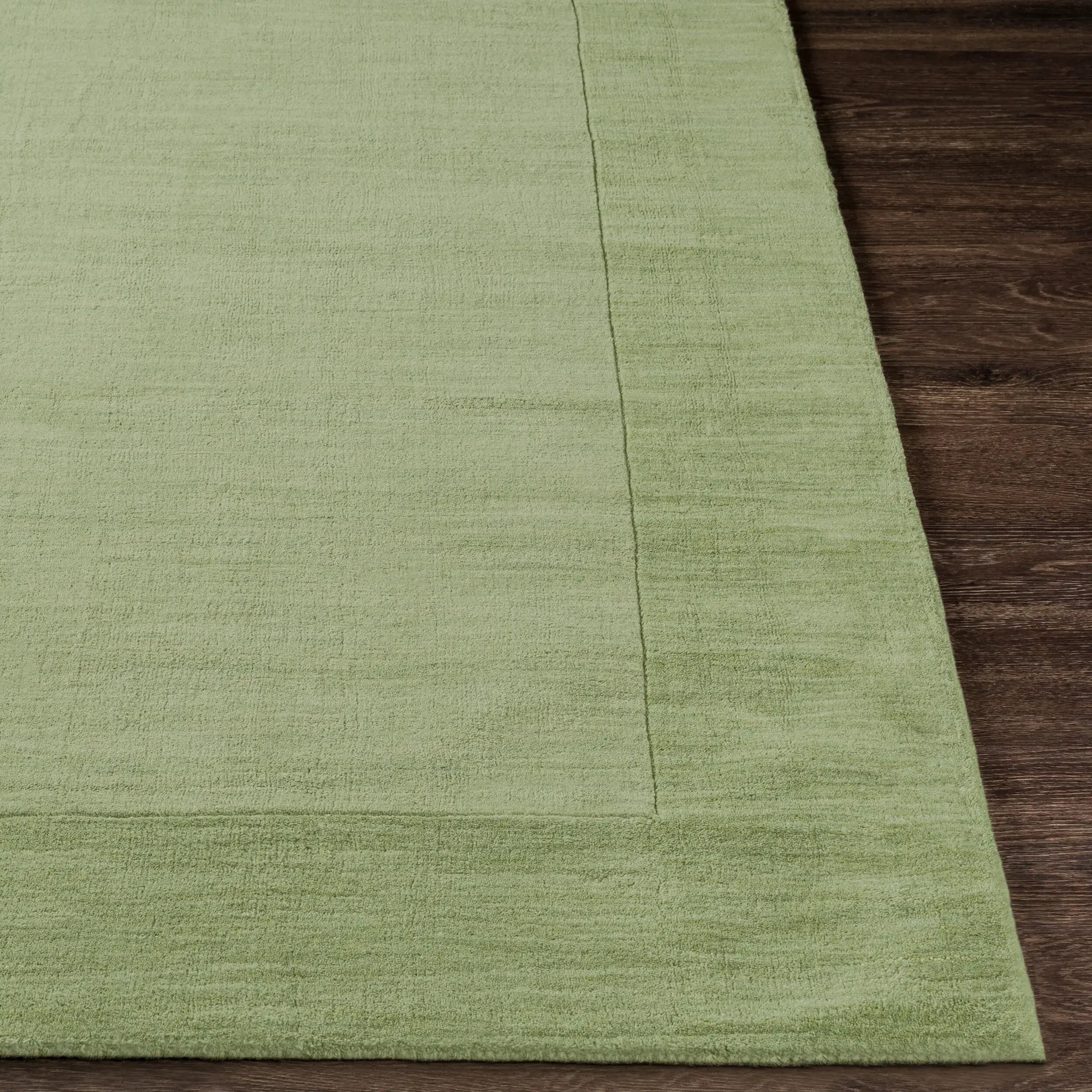 Livabliss Mystique M-310 medium green hand-loomed wool area rug featuring a textured high and low pile design with a subtle border on dark wood flooring.