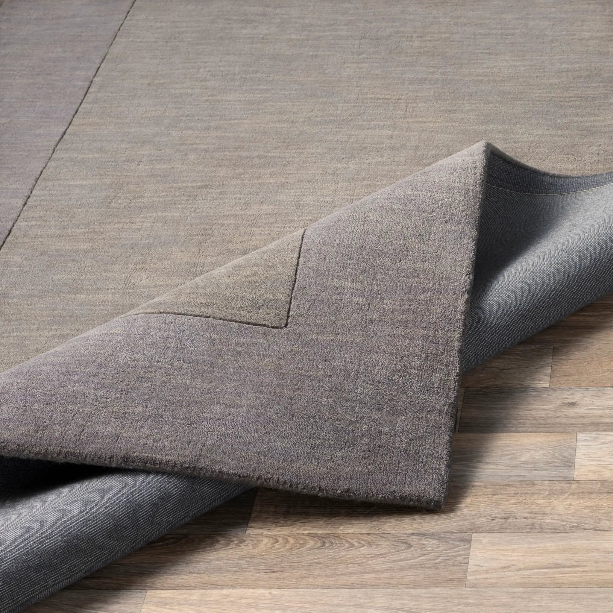 Livabliss Mystique M-312 charcoal wool area rug with textured high/low pile and geometric detail, folded on wood flooring.