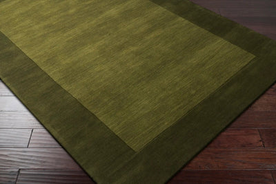 Livabliss Mystique M-315 Olive area rug featuring a two-tone design with a lighter center and darker border, showcasing a textured wool pile on hardwood flooring.