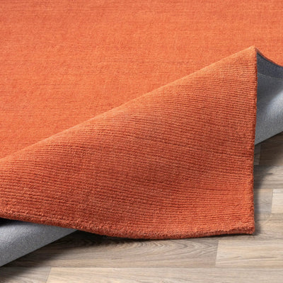 Livabliss Mystique M-332 Burnt-Orange, hand-crafted wool area rug with a textured high-low pile weave and grey backing, corner folded on a wood floor.