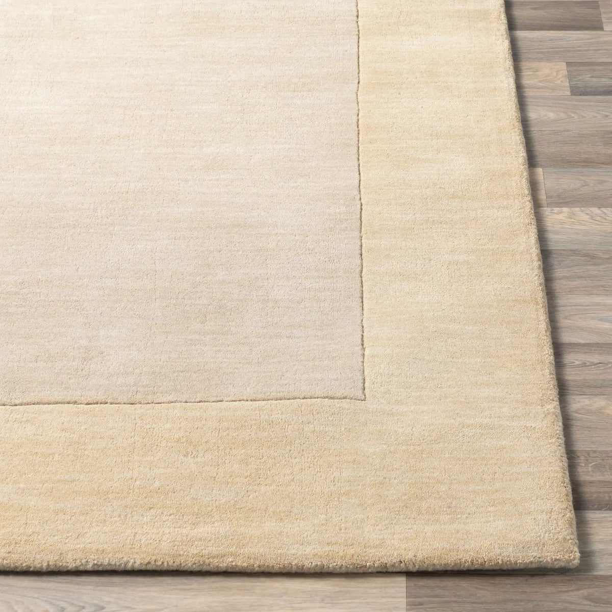 Close-up detail of a Livabliss Mystique M-344 beige area rug corner showing a lighter field, textured border, and hand-loomed wool construction on wood flooring.