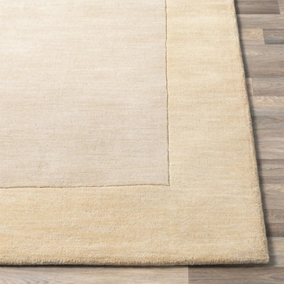 Close-up detail of a Livabliss Mystique M-344 beige area rug corner showing a lighter field, textured border, and hand-loomed wool construction on wood flooring.