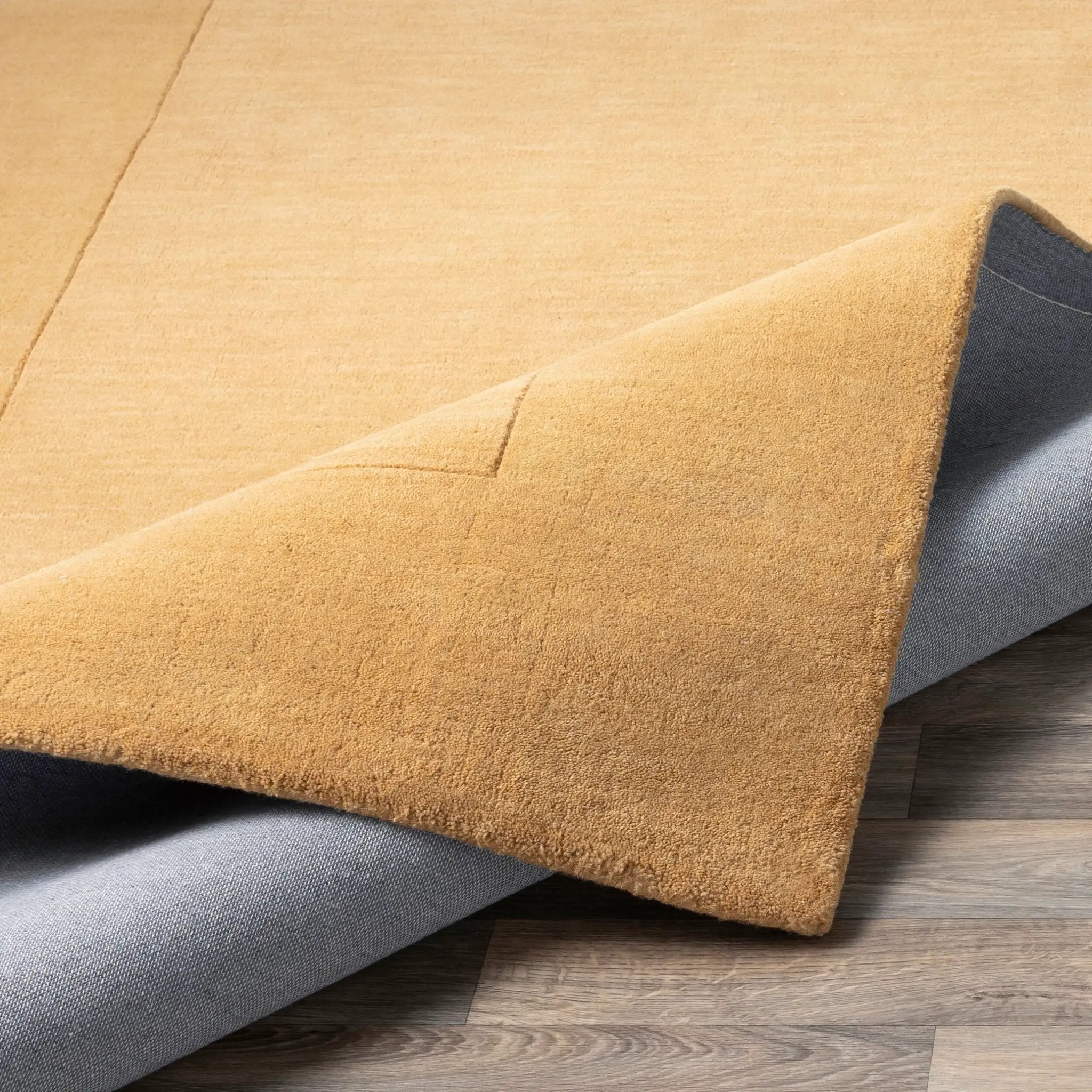 Textured Livabliss Mystique M-345 camel color area rug, folded to show plush pile and subtle surface pattern on wood flooring.