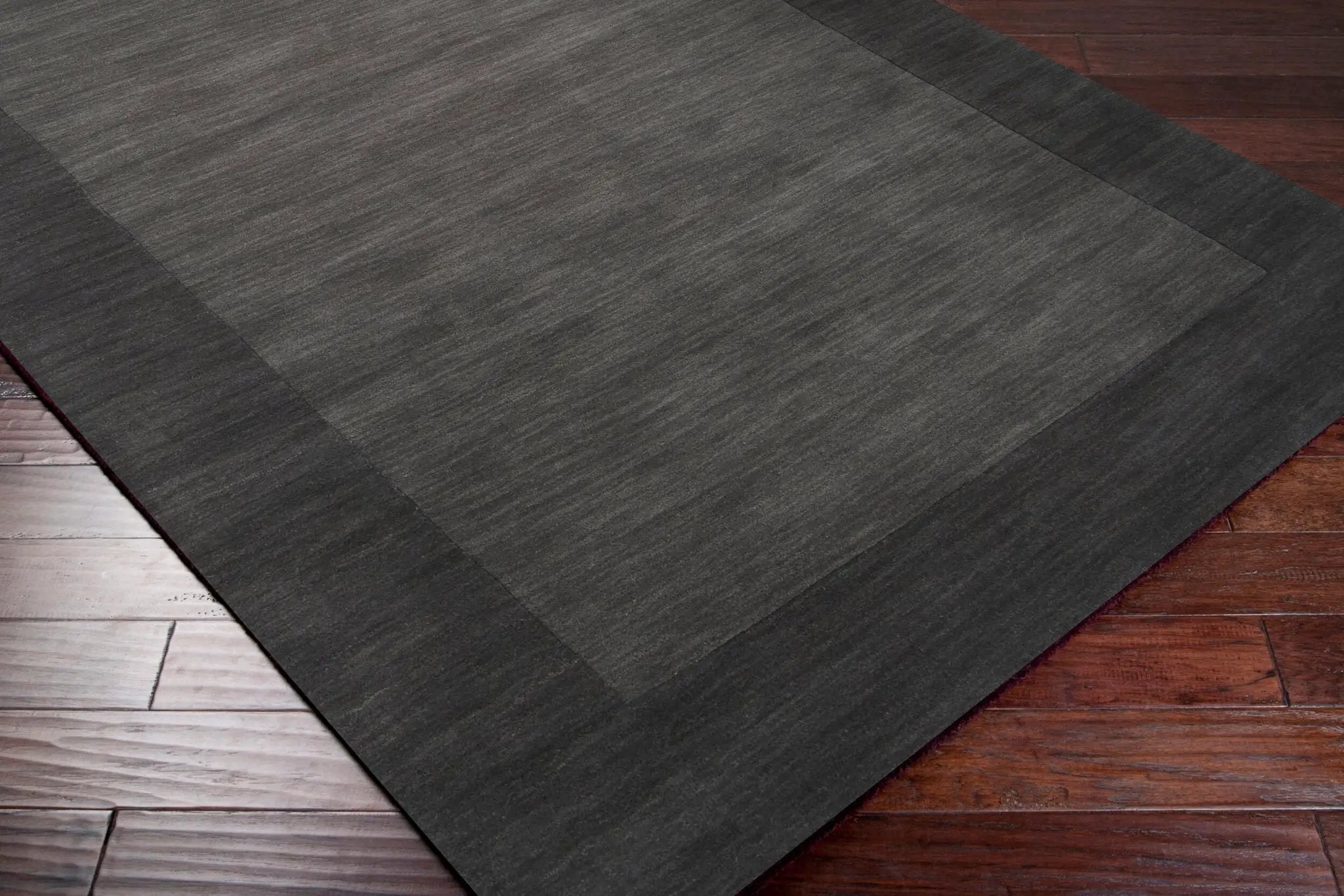 Livabliss Mystique M-347 Charcoal area rug with textured center and darker border laid on hardwood floor for modern living spaces.