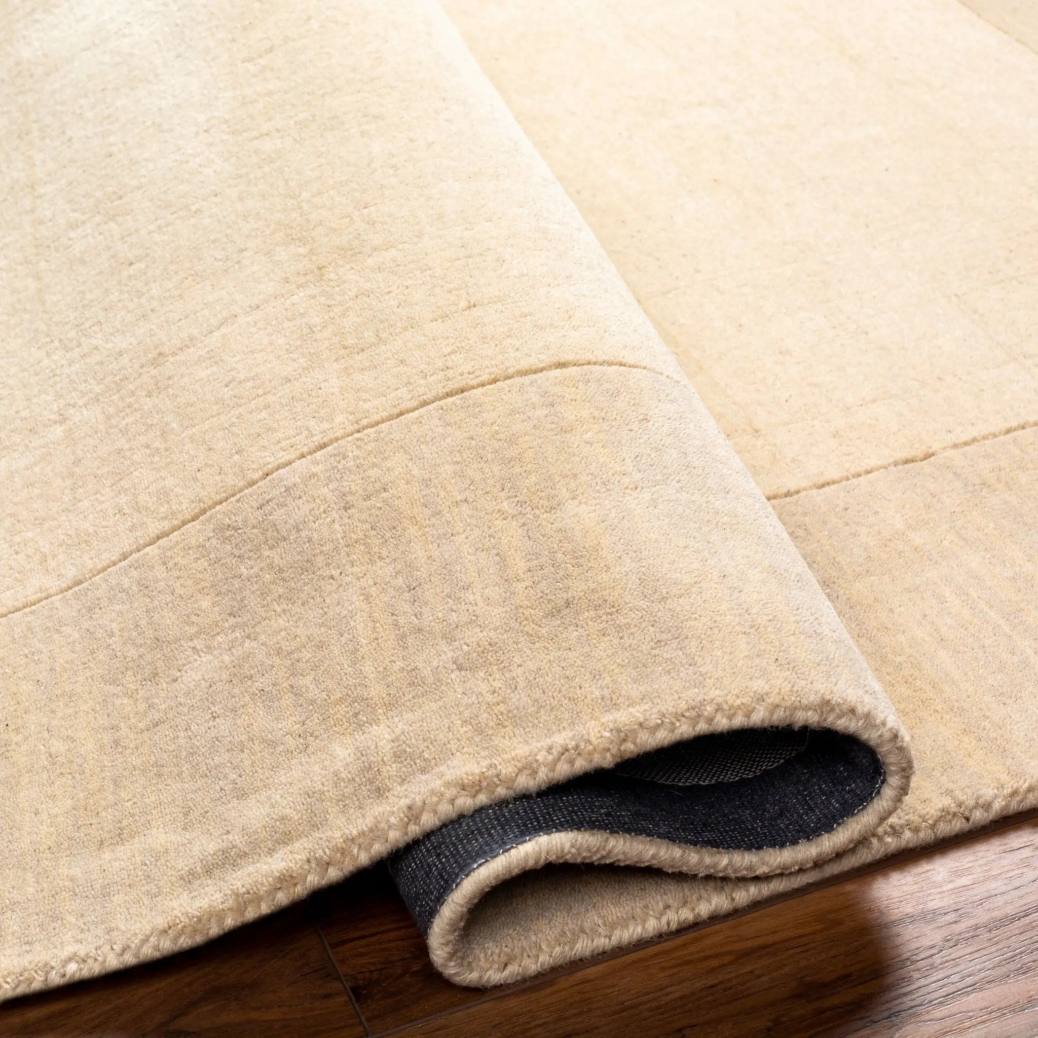 Livabliss Mystique M-348 Cream hand-loomed Indian wool area rug with high-low pile texture, corner rolled to show dark backing on wood floor.