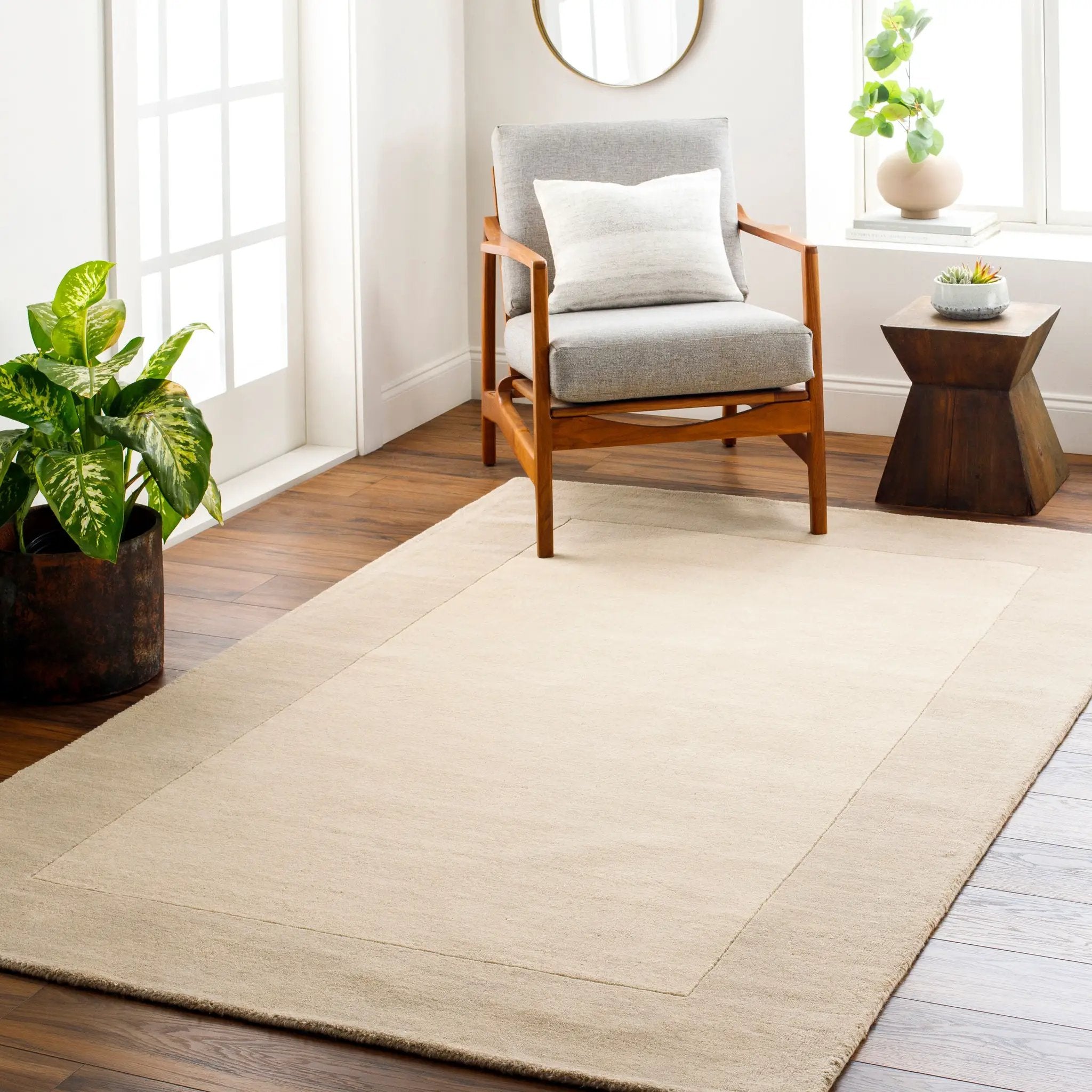 Livabliss Mystique M-348 Cream hand-loomed wool area rug with a high-low pile border, styled under a wooden armchair in a bright contemporary living space.