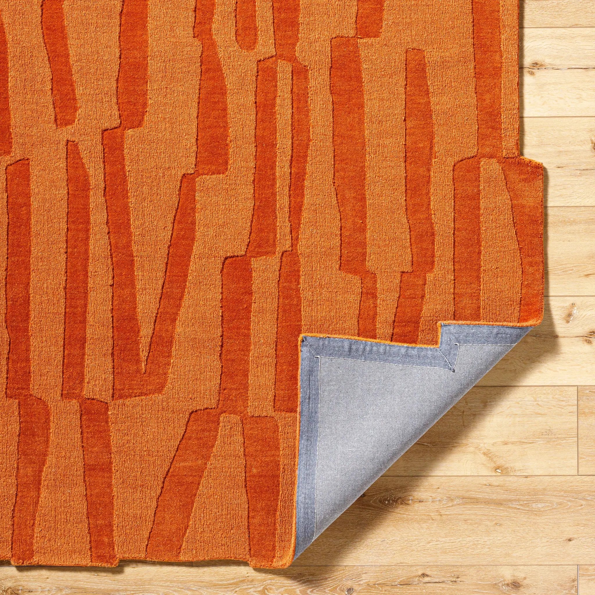Livabliss Mystique M-5488 Burnt sienna hand-loomed wool area rug with abstract texture, corner folded to show grey backing on wood floor.