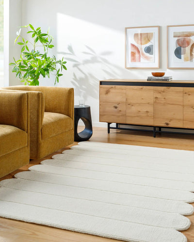 Livabliss Hand Loomed Mystique M-5492 Ivory area rug with unique scalloped edges and textured stripes lies on hardwood floors beside a mustard armchair and wooden sideboard in a sunlit living room.