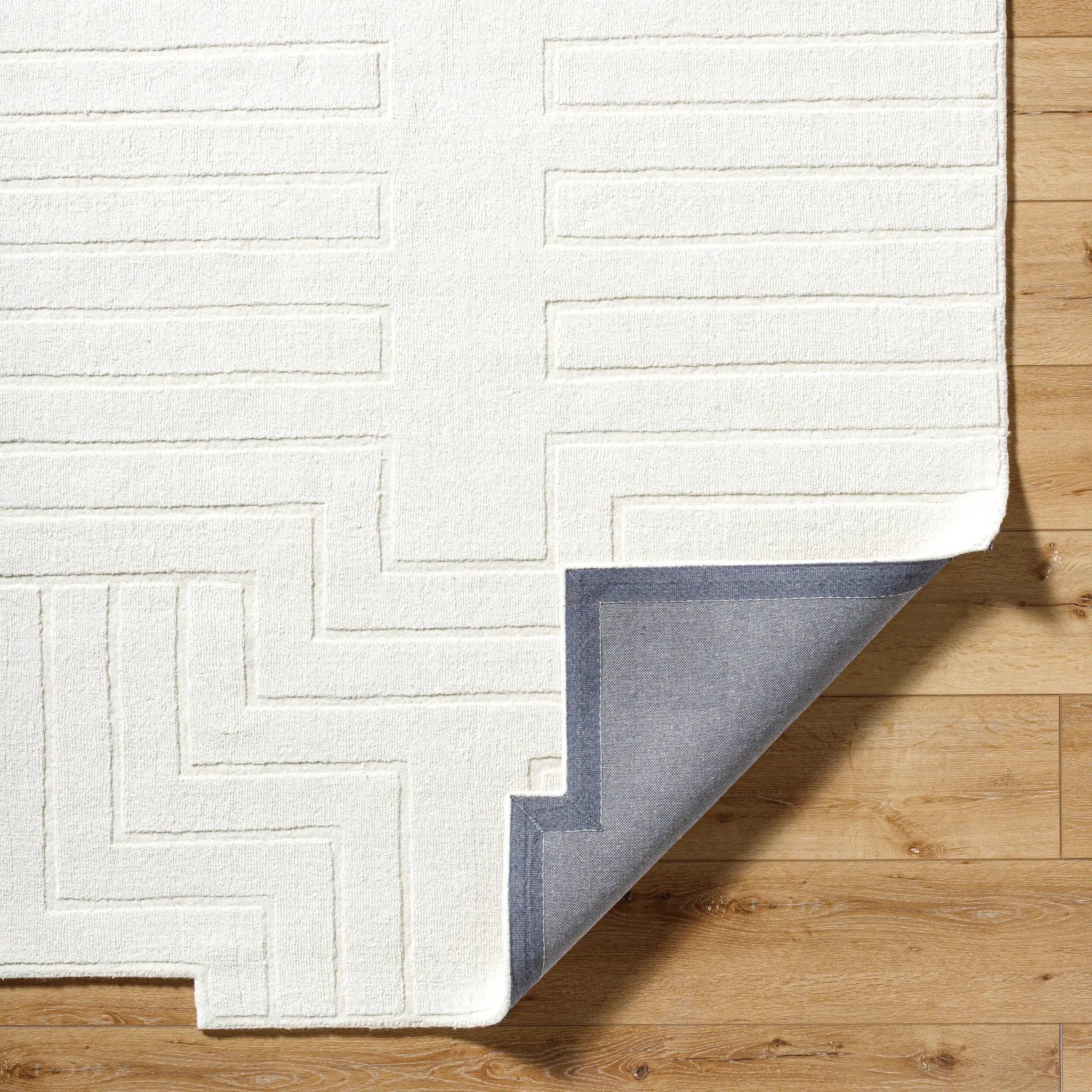 Livabliss Mystique M-5498 Ivory hand-loomed wool area rug with embossed geometric lines and grey backing corner on wood floor.